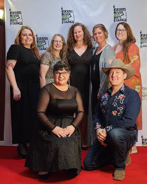 Arts council members posing on a red carpet with film director and film featured artist a film screening event. 